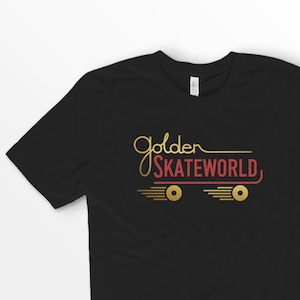 Może przedstawiać: Czarny T-shirt z grafiką w kolorze złotym i czerwonym, na której widnieje napis "Golden Skateworld" oraz stylizowany projekt deski skateboardowej.