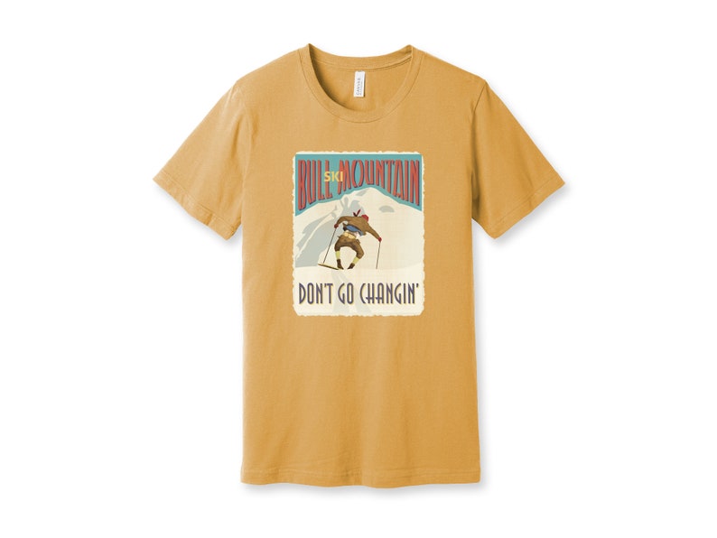 K&ouml;nnte beinhalten: Ein senfgelbes T-Shirt mit einer Grafik im Vintage-Stil eines Skifahrers auf einem Berg. Die Grafik lautet "Bull Mountain Ski" und "Don't Go Changin'".