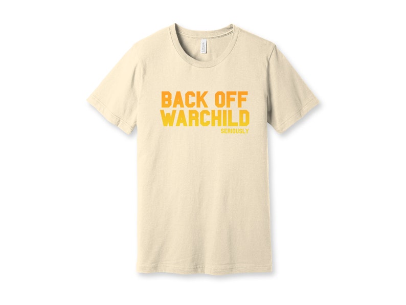 May include: A beige t-shirt with the text "Back Off Warchild Seriously" printed in orange and yellow.