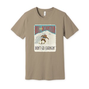 K&ouml;nnte beinhalten: Ein beiges T-Shirt mit einer Grafik im Vintage-Stil eines Skifahrers auf einem Berg. Die Grafik lautet "Bull Mountain Ski" und "Don't Go Changin'."