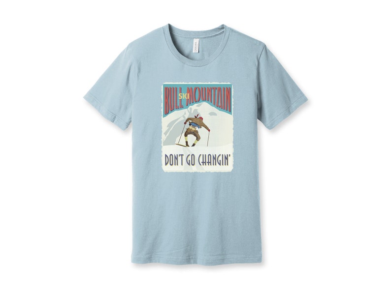 K&ouml;nnte beinhalten: Ein hellblaues T-Shirt mit einer Grafik im Vintage-Stil eines Skifahrers auf einem Berg. Die Grafik lautet "Bull Mountain Ski" und "Don't Go Changin'."