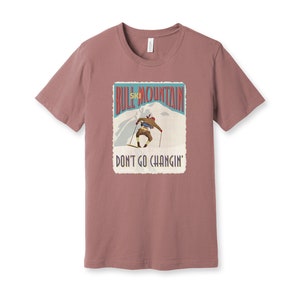 K&ouml;nnte beinhalten: Ein mauvefarbenes T-Shirt mit einer Grafik im Vintage-Stil eines Skifahrers auf einem Berg. Die Grafik lautet "Bull Mountain Ski" und "Don't Go Changin'."