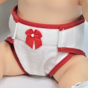 May include: White baby doll diaper with red trim and a red bow with a pearl center. The diaper is made of a soft, absorbent material and is designed to fit a baby doll.