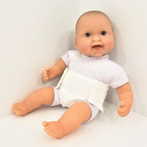 May include: A white baby doll with a white diaper and a white shirt. The doll has a smiling face with blue eyes and a pink complexion.