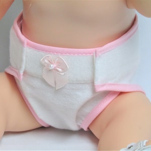 May include: A white diaper with pink trim and a pink bow. The diaper is made of soft, absorbent material and is designed for dolls.