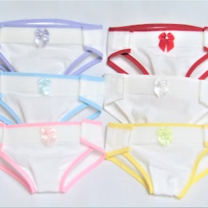 May include: Six pairs of white underwear with different colored trim and a small bow on the front. The colors are purple, red, blue, pink, yellow, and light blue.