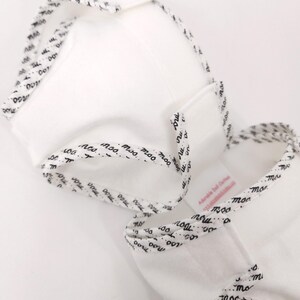 May include: A white baby garment with black text that reads "moo" around the edges. The garment is made of soft fabric and has a simple design. The text is repeated around the edges of the garment.