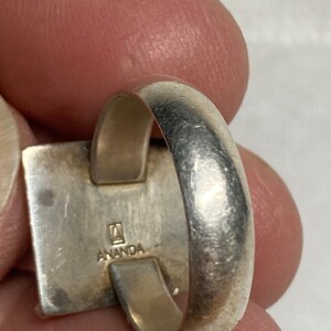 May include: Silver ring with a square design and the inscription "ANANDA" on the side.