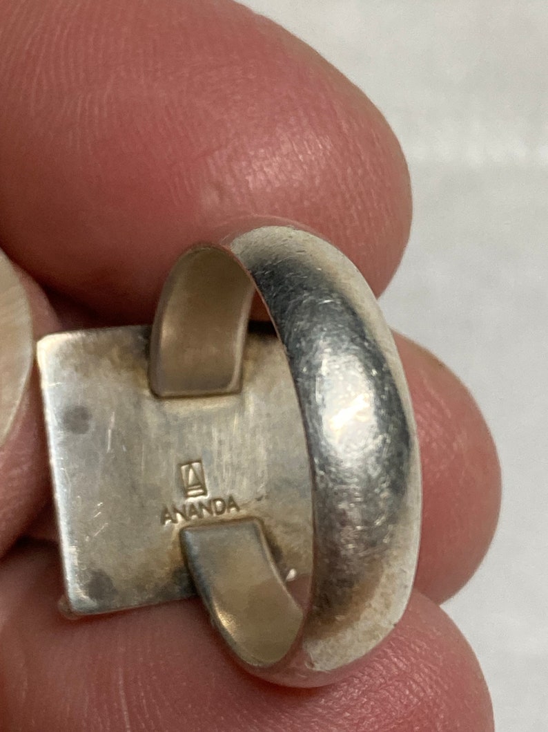 May include: Silver ring with a square design and the inscription "ANANDA" on the side.