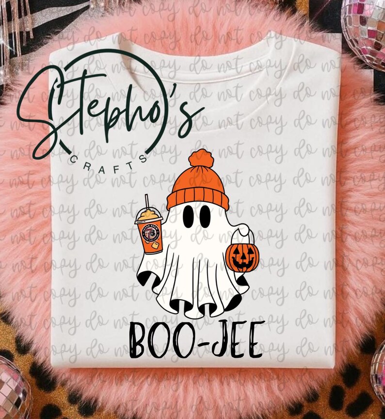 May include: White t-shirt featuring a cartoon ghost wearing an orange beanie and holding a pumpkin bucket and a coffee drink. The text "BOO-JEE" is printed below the ghost. The shirt has the logo "Stepho's Crafts" at the top.