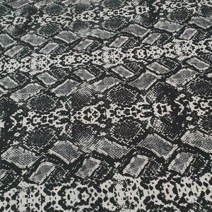 May include: Black and white fabric with a snake skin pattern. The fabric has a subtle sheen and a textured surface.