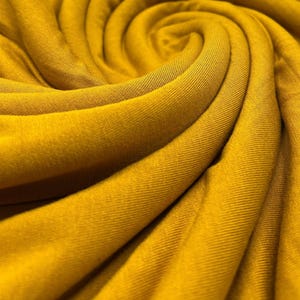May include: Close-up of a soft, yellow fabric with a textured surface. The fabric is folded and draped in a swirling pattern.