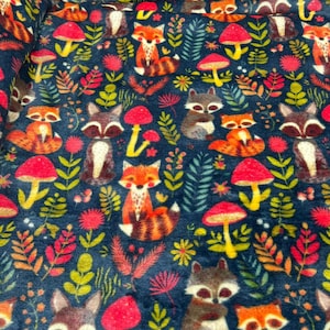 May include: Dark blue fabric with a repeating pattern of woodland animals and plants. The design includes foxes, raccoons, mushrooms, and various leaves and flowers in orange, red, yellow, and green.