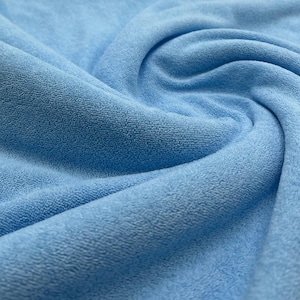 May include: A close-up shot of a light blue fabric with a soft, textured surface. The fabric is arranged in flowing folds, creating shadows and highlights that accentuate its plush texture. The image suggests a comfortable material, perhaps for a blanket or towel.