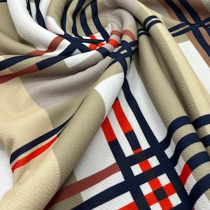 May include: Beige fabric with a plaid pattern in navy blue, red, and brown. The fabric is folded and textured.