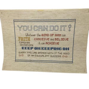 May include: Beige fabric wall hanging with blue, red, and orange embroidered text that reads "YOU CAN DO IT! Whatever the MIND OF MAN can FAITH CONCEIVE and BELIEVE removes it can ACHIEVE limitations KEEP ON KEEPING ON EVERY FAILURE BRINGS WITH IT THE SEED OF AN EQUIVALENT SUCCESS"
