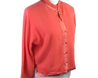 May include: Coral-colored cardigan with a mandarin collar and long sleeves. The sweater features a satin trim along the collar, button placket, and hem. The button-up closure has matching coral buttons.