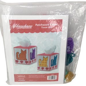 May include: A craft kit for a Patchwork Kitten tissue box. The box design features orange, purple, and blue cat silhouettes, with red hearts. The kit includes yarn and a plastic canvas.