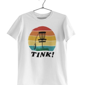 May include: White t-shirt with a retro sunset graphic featuring a disc golf basket and the text "TINK!"