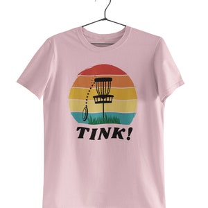 May include: Pink t-shirt with a retro sunset graphic featuring a disc golf basket and the text "TINK!"