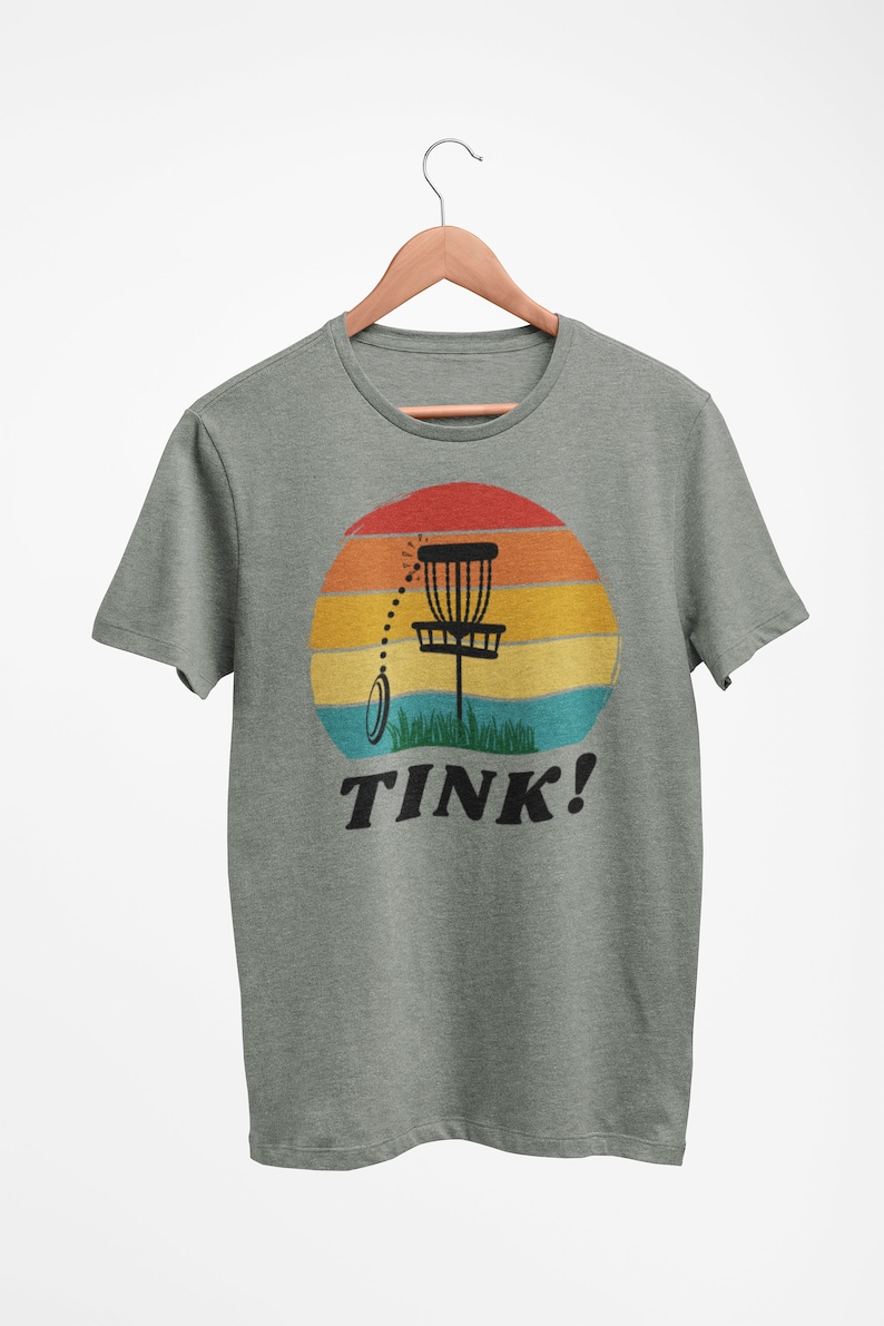 May include: A green t-shirt with a retro sunset graphic featuring a disc golf basket and the text "TINK!"