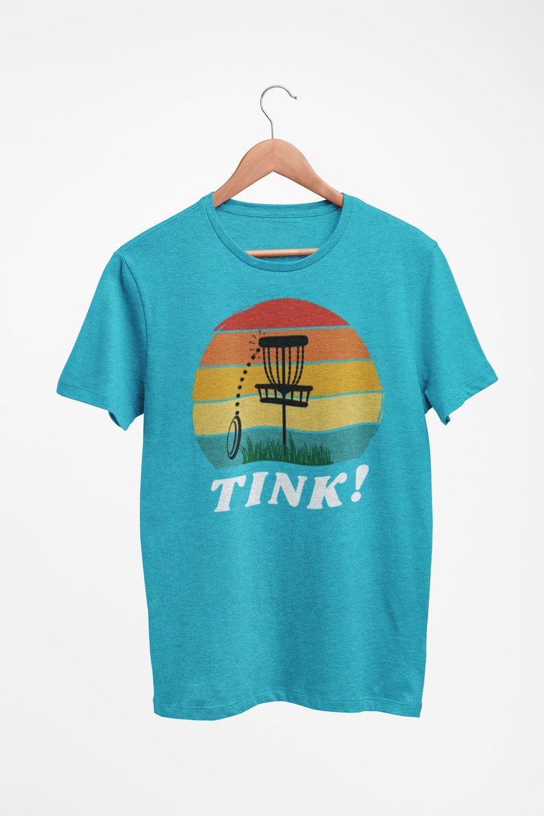 May include: A turquoise blue t-shirt with a retro sunset graphic featuring a disc golf basket and the text "TINK!"