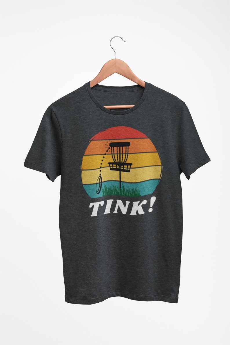 May include: A dark grey t-shirt with a retro sunset graphic featuring a disc golf basket and the text "TINK!"