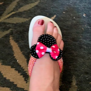 May include: White flip-flop sandals with black and white polka dot bow embellishment. The sandals have a pink bow with white polka dots.