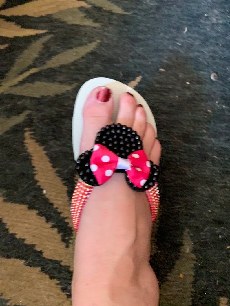 May include: White flip-flop sandals with black and white polka dot bow embellishment. The sandals have a pink bow with white polka dots.