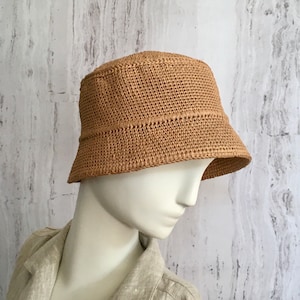 May include: A tan crocheted bucket hat with a wide brim. The hat is made of a woven material and has a simple design.