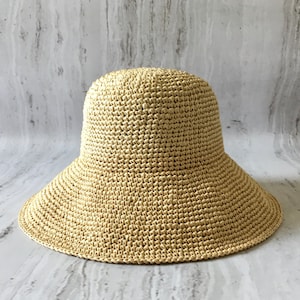 May include: A wide-brimmed straw hat in a light beige color. The hat is crocheted with a fine weave and has a slightly rounded crown.