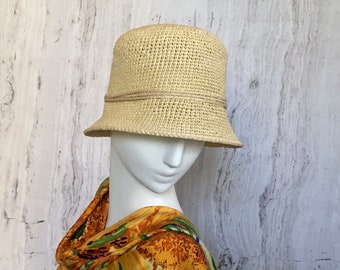 May include: A crocheted straw sun hat in a light beige color with a brown ribbon trim. The hat is on a white mannequin head.
