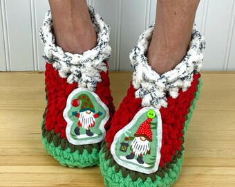 Puede incluir: Pantuflas de crochet rojas, verdes y blancas con una aplicación de gnomo. El gnomo lleva un gorro rojo y tiene barba blanca.