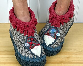 Puede incluir: Un par de zapatillas de crochet grises, azules y rojas con una aplicación de cara de gnomo. Las zapatillas tienen un puño de crochet rosa.