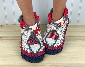 Puede incluir: Pantuflas de crochet con una aplicación de gnomo. Las pantuflas están hechas con una variedad de colores, incluyendo rojo, blanco, gris y negro. La aplicación de gnomo tiene un gorro rojo, barba blanca y ojos negros.