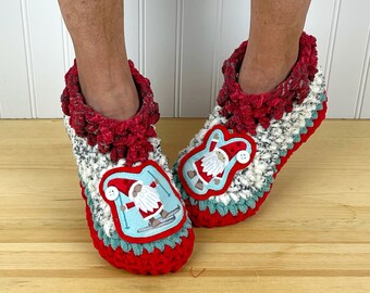 Puede incluir: Pantuflas de crochet rojas y blancas con un puño rojo peludo y una aplicación azul y blanca de un gnomo esquiando.