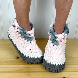 May include: A pair of pink, white and grey crocheted slippers with a fluffy texture.