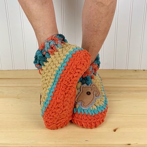 May include: Two crocheted slippers in orange, tan, and teal with a brown felt applique on one slipper.