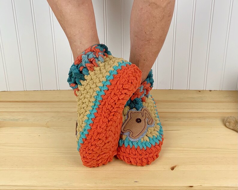 May include: Two crocheted slippers in orange, tan, and teal with a brown felt applique on one slipper.