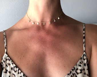 May include: A gold chain choker necklace with small, clear stones dangling from it. The necklace is worn by a person with a light complexion and a leopard print top.