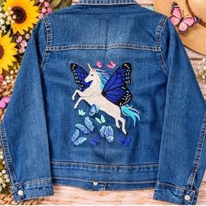 May include: A blue denim jacket featuring a large embroidered design on the back. The embroidery depicts a white unicorn with blue butterfly wings, surrounded by several smaller blue and pink butterflies. The jacket has long sleeves and buttons.