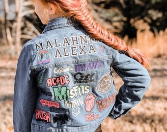 May include: A blue denim jacket with a variety of band patches, including AC/DC, Misfits, Nirvana, and Kiss. The jacket has the names "MALAHNI ALEXA" embroidered on the back.