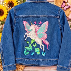 May include: A blue denim jacket featuring a large embroidered design on the back. The embroidery depicts a white unicorn with pink hair and large teal and pink butterfly wings, surrounded by several smaller green and blue butterflies.