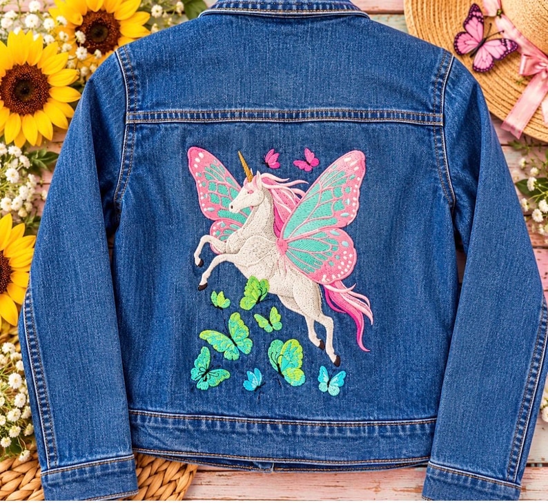 May include: A blue denim jacket featuring a large embroidered design on the back. The embroidery depicts a white unicorn with pink hair and large teal and pink butterfly wings, surrounded by several smaller green and blue butterflies.