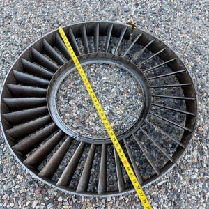 May include: A circular metal turbine fan with angled blades. A yellow measuring tape is laid across the fan, showing a diameter of approximately 38 inches. The fan is made of a dark, possibly steel, material.