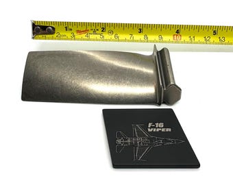 May include: A metal turbine blade next to a black F-16 Viper graphic. The blade is approximately 4 inches long. A yellow tape measure is in the background.