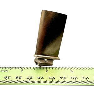 Può includere: Una pala di turbina in metallo dorato che misura circa 5 cm di lunghezza. La pala è appoggiata su un righello con segni in pollici.