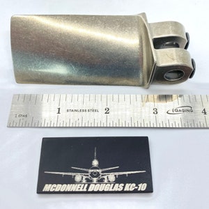 May include: A metallic silver-colored aircraft part with a ruler showing inches. A black rectangular plaque with a white illustration of an airplane and the text "MCDONNELL DOUGLAS KC-10" is below the ruler.