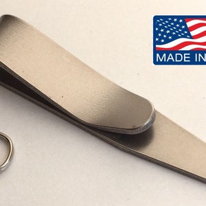 May include: A silver metal money clip with a rounded edge and a small ring on the end. The clip is made in the USA.