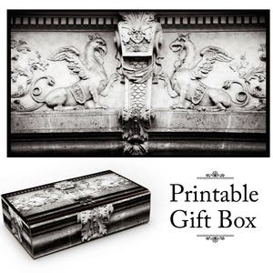 Peut inclure: Une boîte cadeau imprimable en noir et blanc avec un motif décoratif représentant deux créatures ailées et des volutes ornées. Le texte "Boîte cadeau imprimable" est imprimé sur le devant de la boîte.